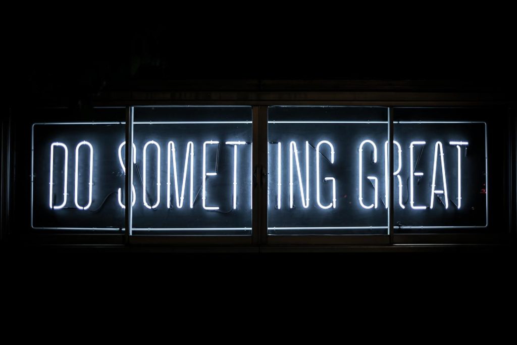 A neon sign with the message 'DO SOMETHING GREAT' on a black background, inspiring viewers to take bold actions and achieve their goals.